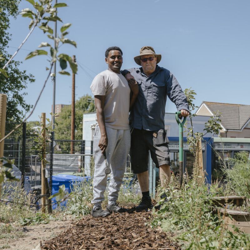 2 men stood in a garden space with tools