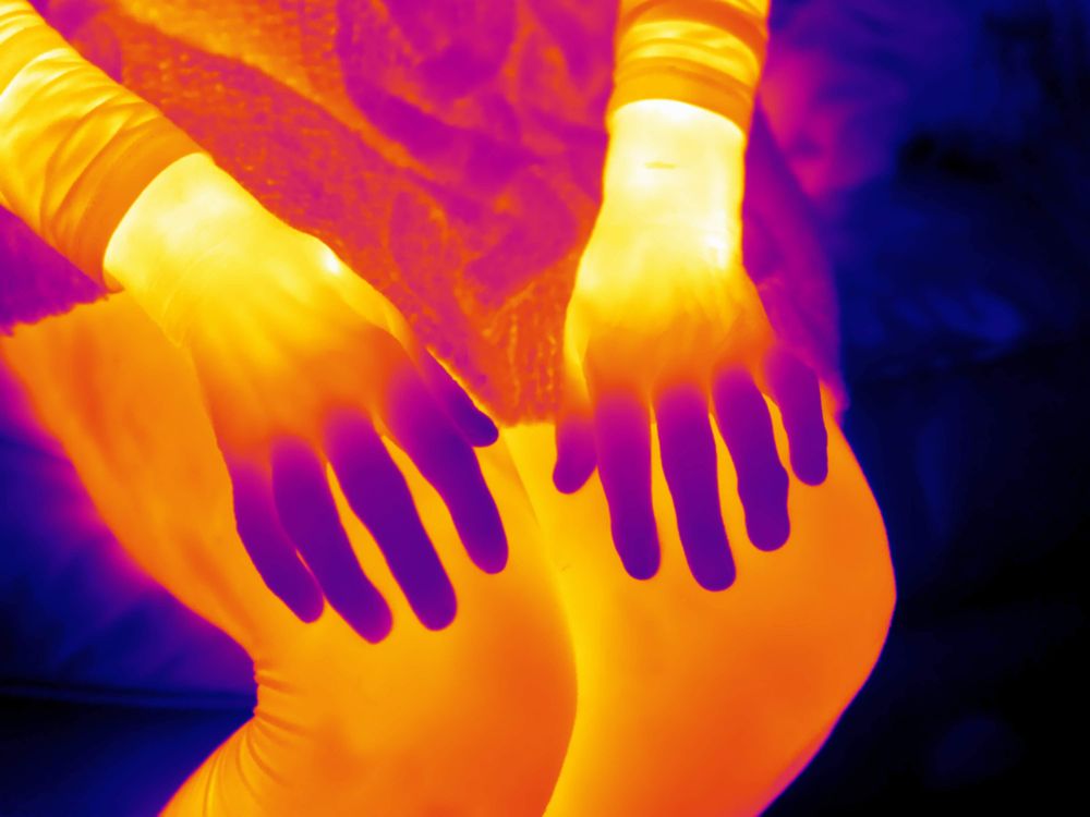 Thermal image of a womans hands glowing yellow but with cold fingers in blue.