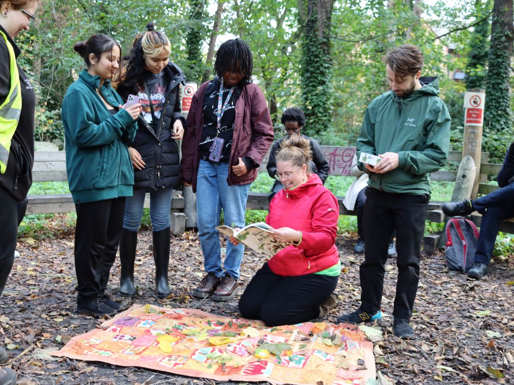 A group of young people stand round a staff member kneeling on the ground, looking at a colourful poster