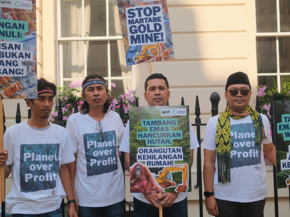 Friends of the Earth Indonesia members wearing t-shirts which read planet over profit, holding banners which read "stop Martabe gold mine"