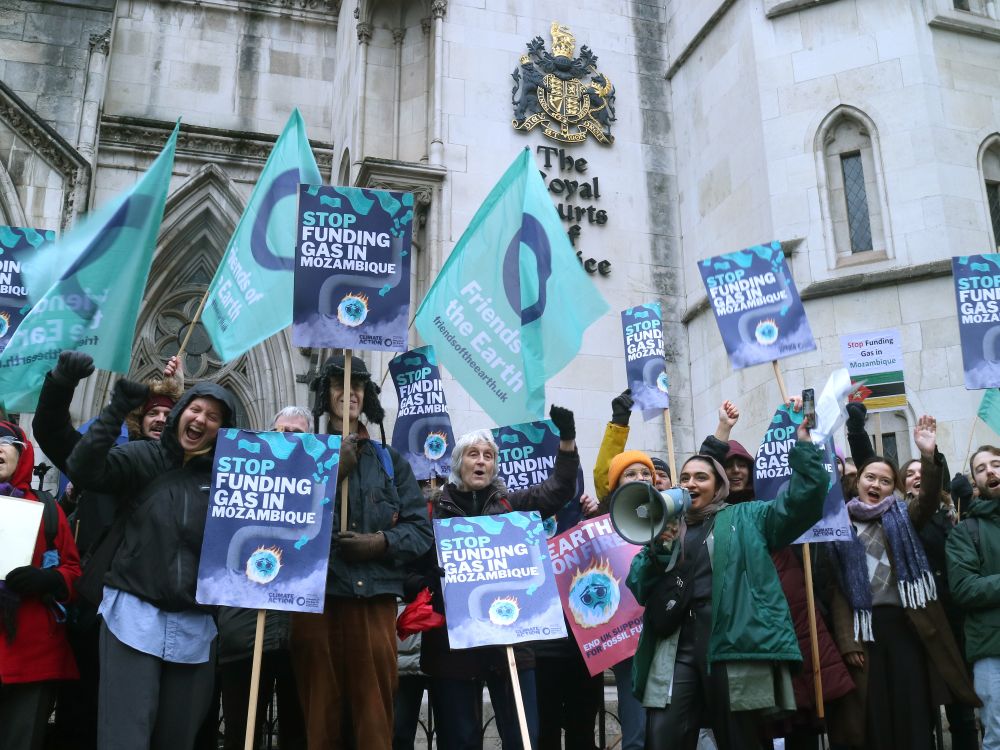 A group of climate protesters of different ages and ethnicities standing outside the Royal Courts of Justice with placards reading "Stop funding gas in Mozambique"