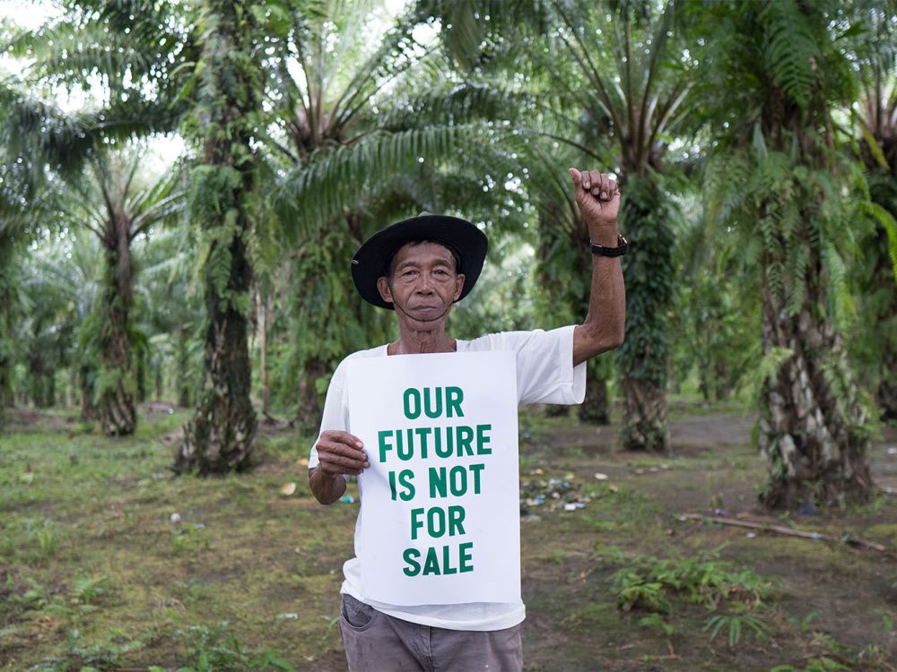 Man stands in forest with fist raised, holding a sign that reads: Our future is not for sale