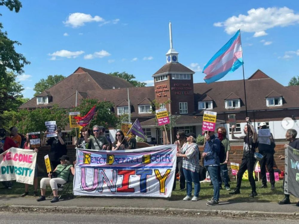 A group of people demonstrate in front of a hotel holding placards and banners that say things like "Reject prejudice, foster unity," "Welcome diversity" and "Refugees welcome, stop the far right"