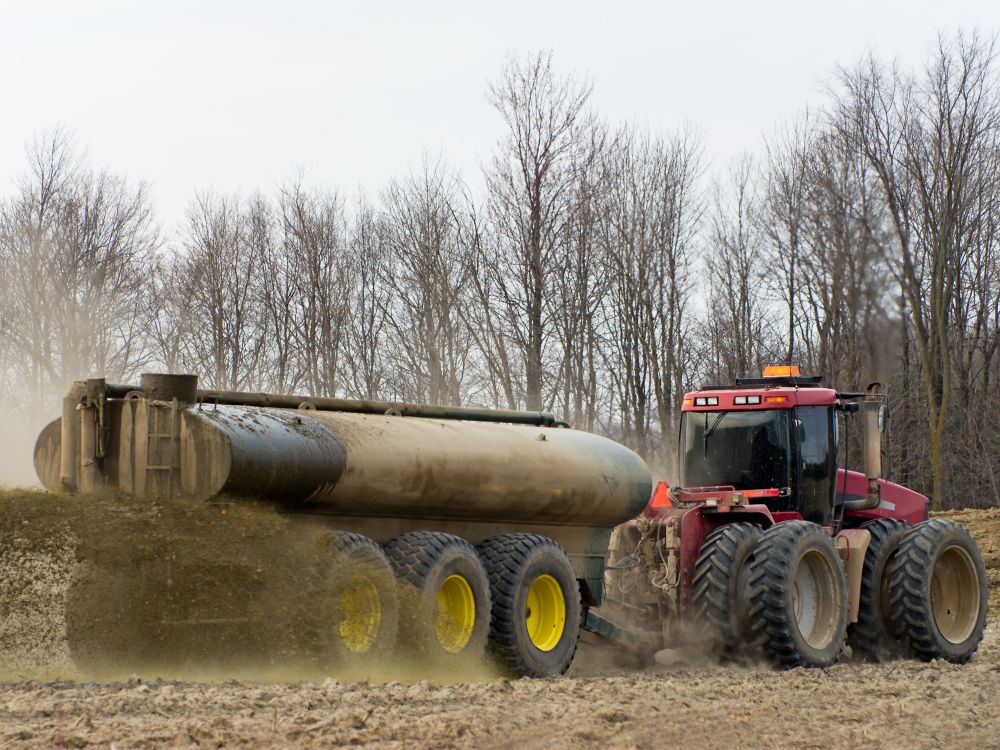 A large tractor drives across a field spraying manure on it