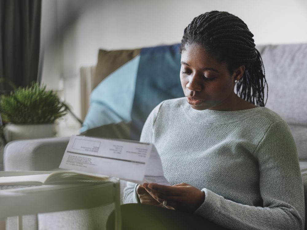 Woman sat by sofa reading paper utility bill