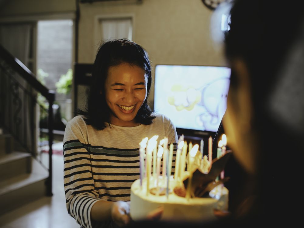 A woman holding a birthday cake with lots of candles on it, she's smiling