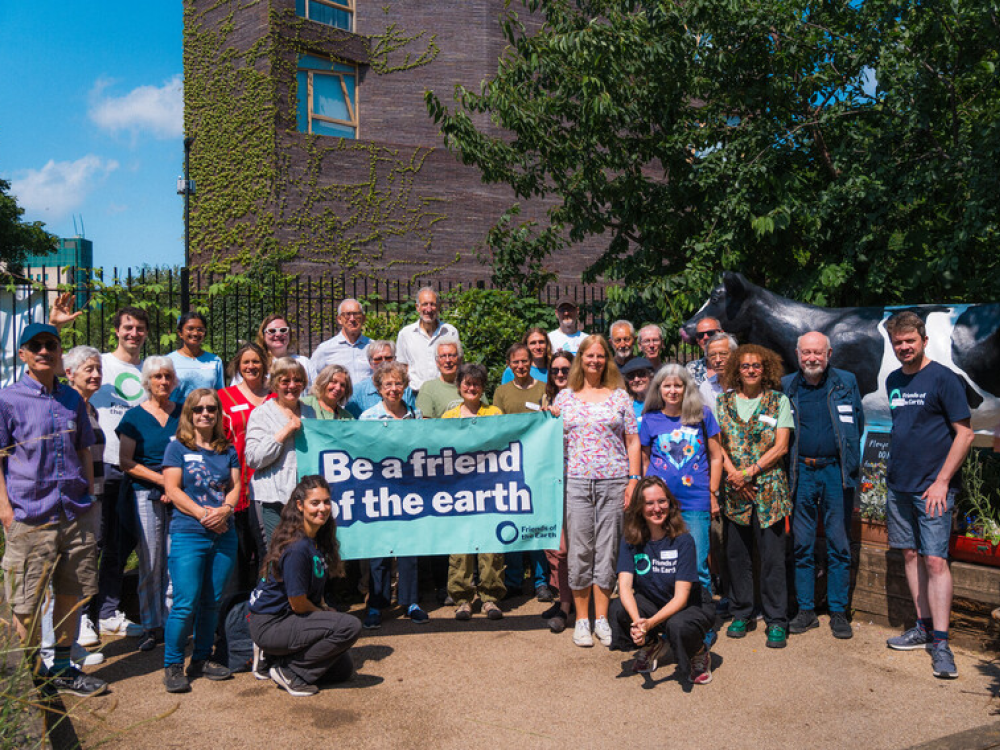 A group of people stand outside a building holding a sign that reads 'Be a friend of the earth'